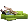 Ein Mann, der auf einem grünen Sofa liegt, hält spielerisch die Hand einer Frau, die über ihm steht. Drei Kissen liegen verstreut auf dem Boden.