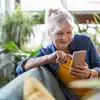 Lächelnde ältere Frau, die zu Hause auf dem Sofa sitzt und ihr Smartphone benutzt