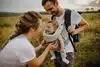 Foto einer jungen, liebevollen Familie, die gerne Zeit miteinander verbringt, draußen mit ihrem Baby, das in einer Babytrage sitzt.