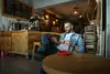 Man sits in a cozy cafe, holding a cup of coffee and looking at his phone.