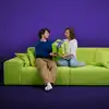 Auf dem Bild sieht man zwei Personen mit einem Geschenk auf dem grünen Sofa von Pax sitzen.